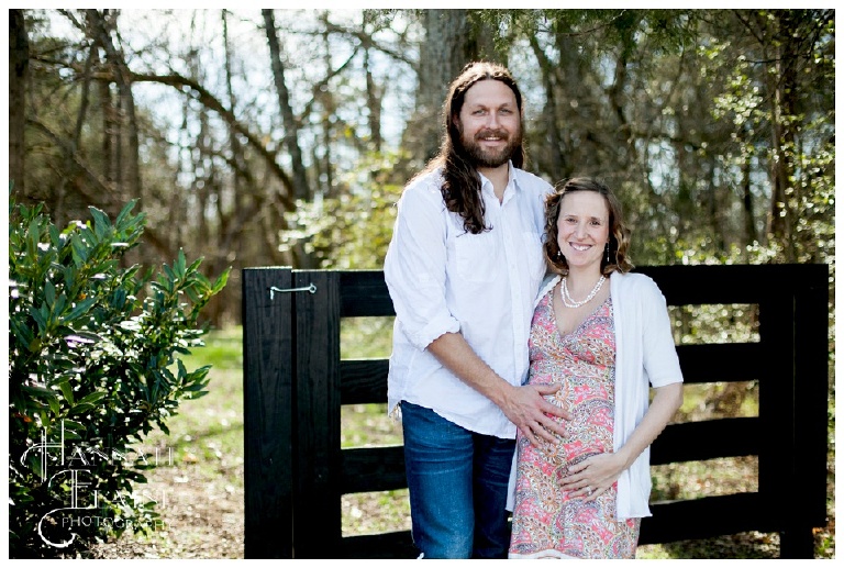 a pregnant couple smiles in front of black gate at arrington vineyards
