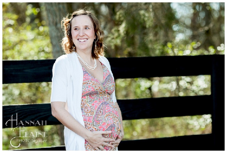a pregnant woman smiles in front of black fence in franklin