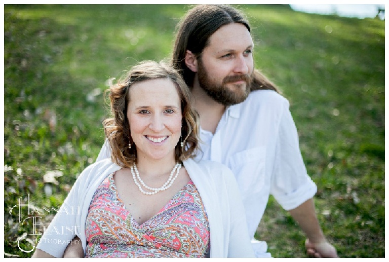 pregnant wife and bearded husband sit in a field