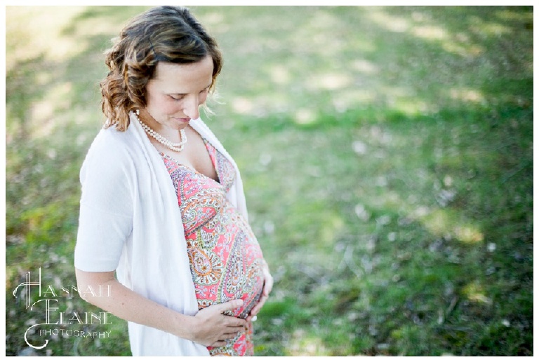 a pregnant woman touches her belly in a spring field