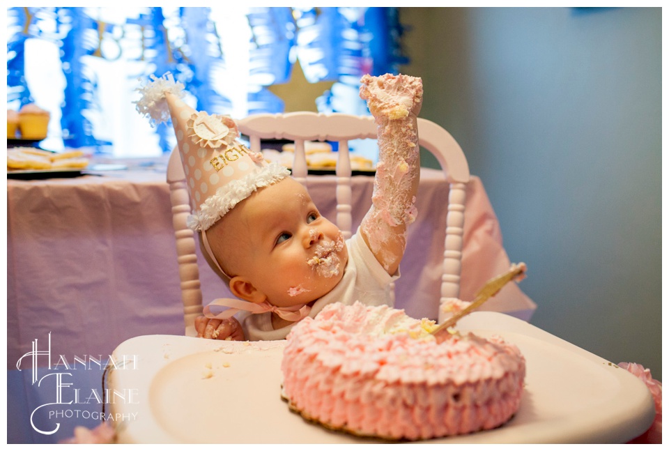 baby does a fist pump covered in icing from her first birthday cake