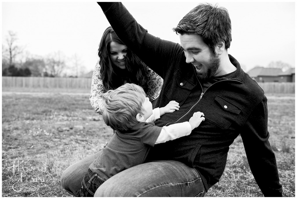 toddler boy tackles his dad to the ground while mom smiles behind