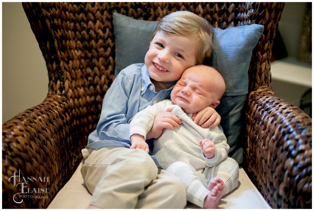 big brother holds his newborn baby brother in a wicker chair