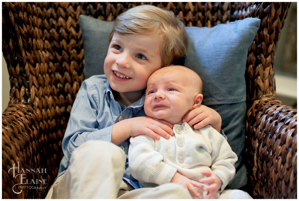 toddler cuddles baby brother in brown chair