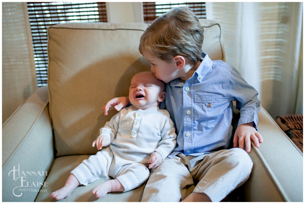 a boy kisses his newborn crying brother on the head