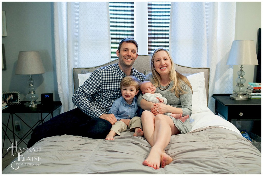 family and new baby sit together on mom and dad's bed