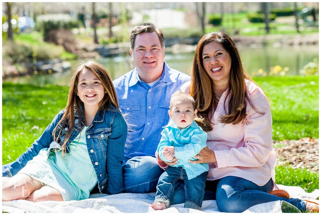 a family of four sits on a white blanket in the park