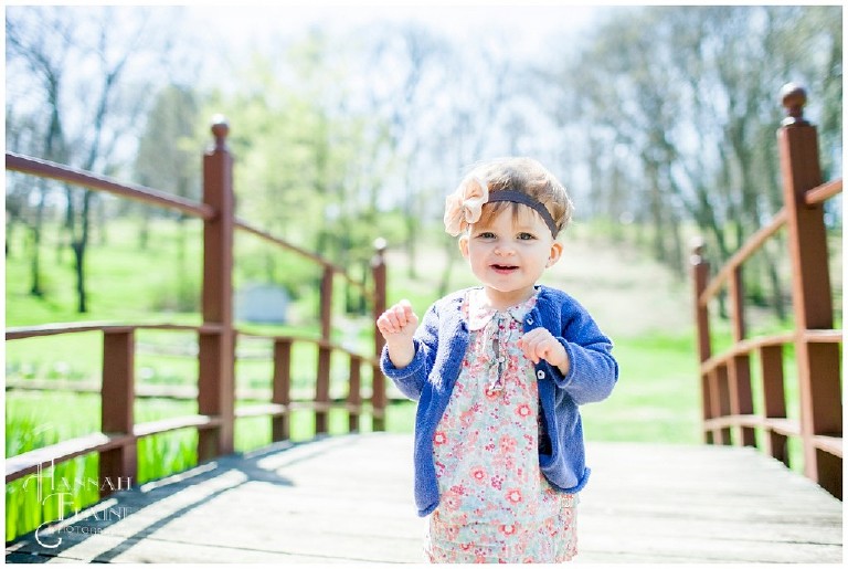 little girl in cardigan stands on a bridge in the iris garden