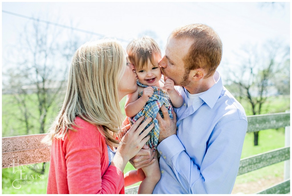 mom and dad kiss baby girl on the cheek