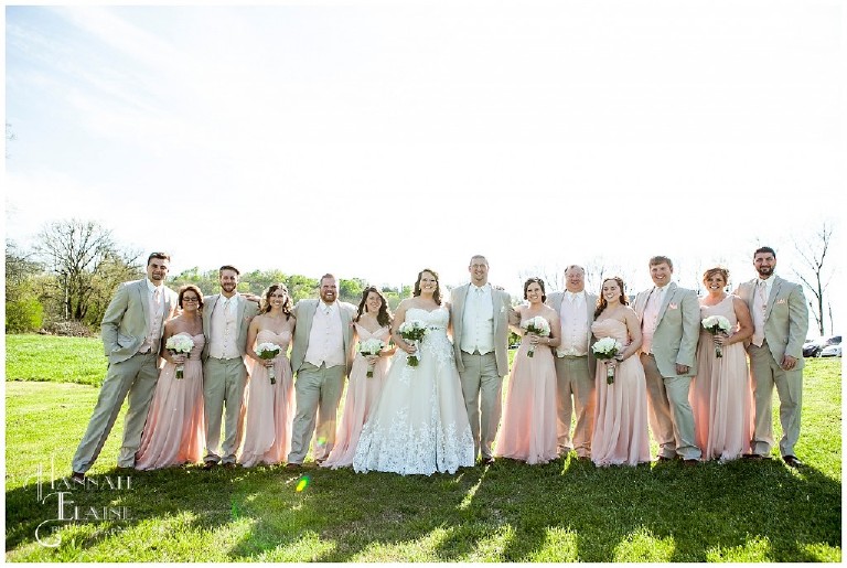 a bridal party stands together in a field in blush and tan