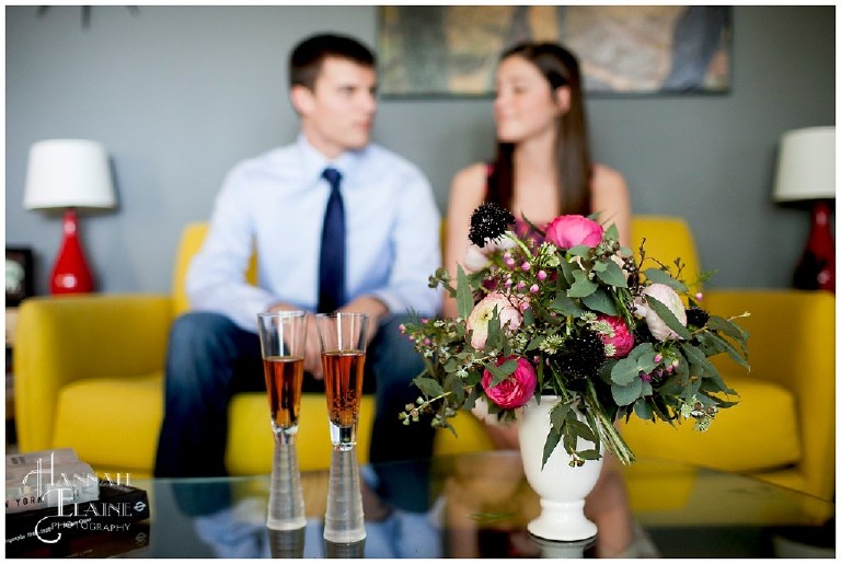 mod champagne flutes and pink spring florals in the foreground, couple behind