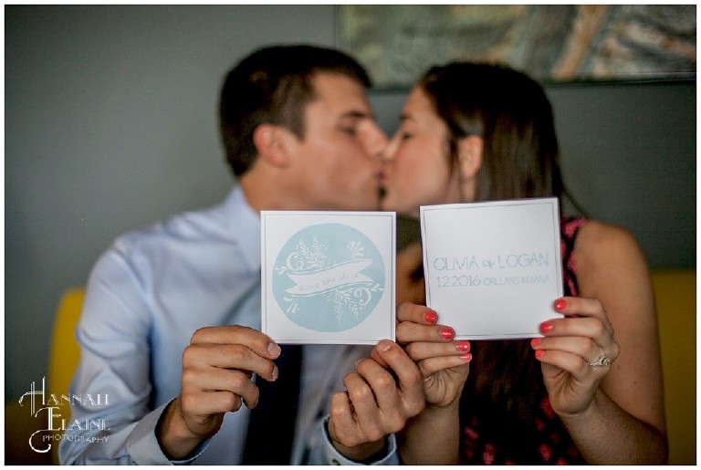 a couple kisses while holding out their double sided save the date cards