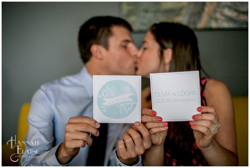 a couple kisses while holding out their double sided save the date cards