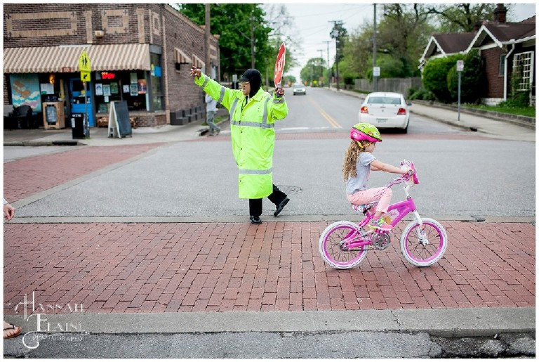 crossing guard helps girl on bike cross the street in front of sky blue cafe