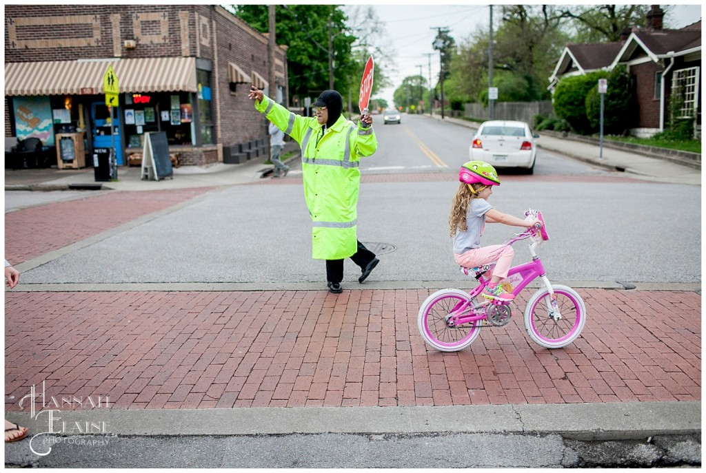 crossing guard helps girl on bike cross the street in front of sky blue cafe