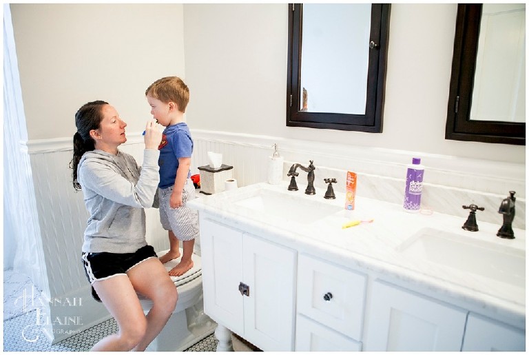 boy stands on the toilet while mom helps him brush his teeth