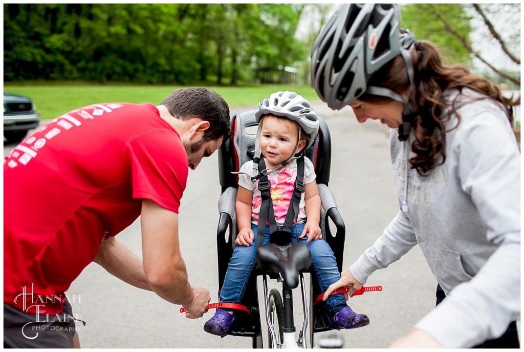 mom and dad strap baby into the kid seat on the bike