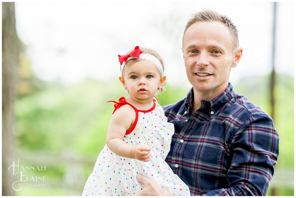 little girl in white dress and red bow in her dad's arms