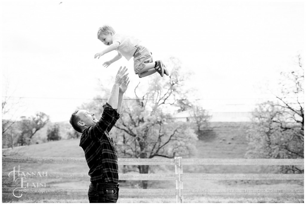 dad throws son up in the air in front of white fence