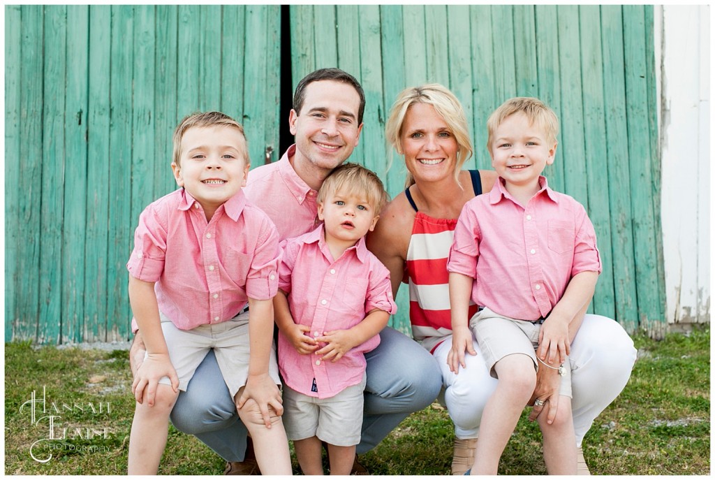 family stands in front of teal rustic barn door