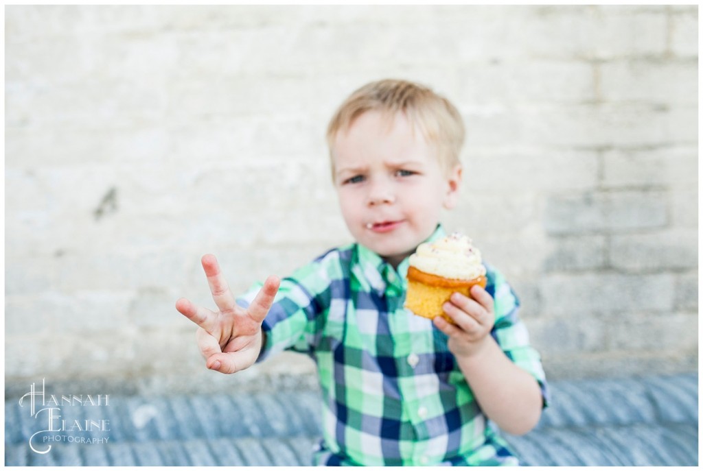 boy holds up 3 fingers to show his age in between bites of his whole foods cupcake