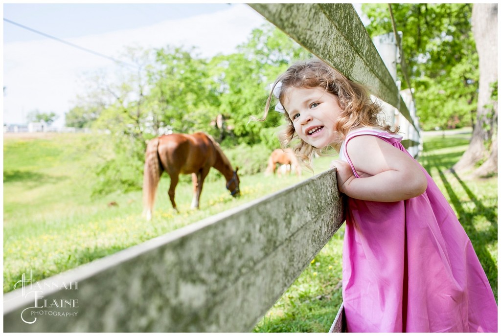 little girl pokes her head through the fence to talk to the metro police horses