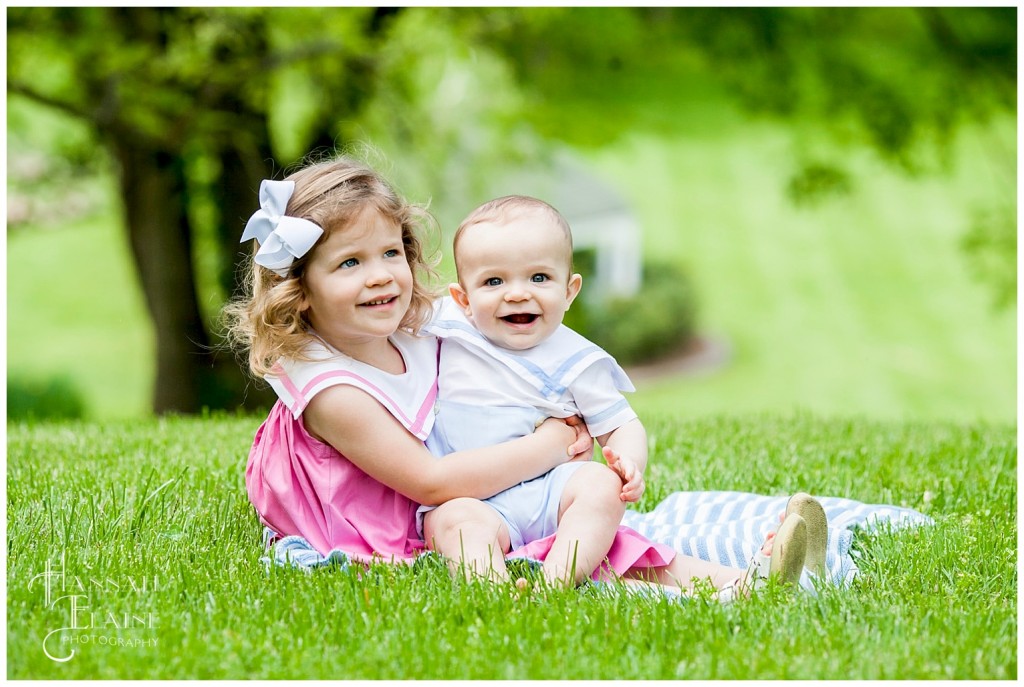 big sister holds little brother on her lap in the park