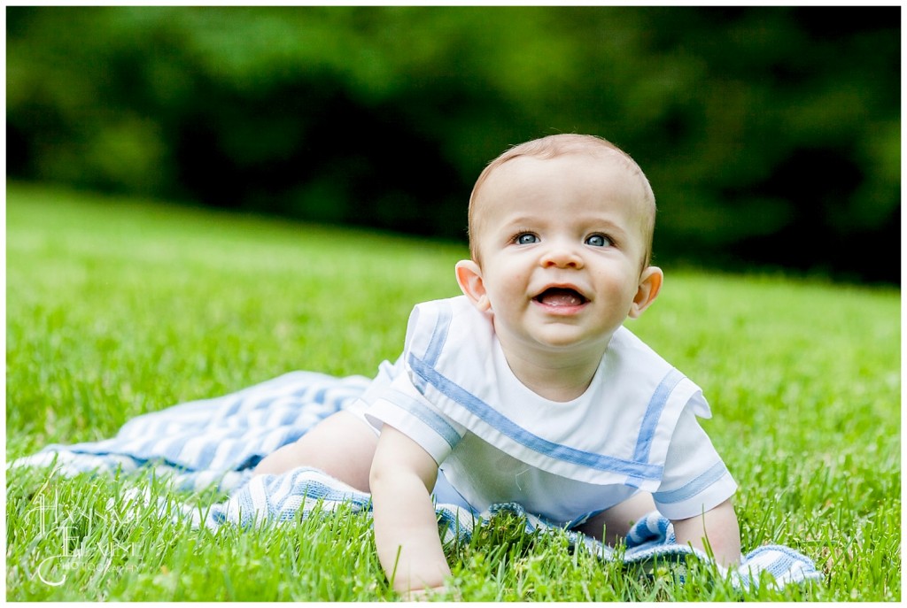 little boy tries to crawl off his blanket in the grass