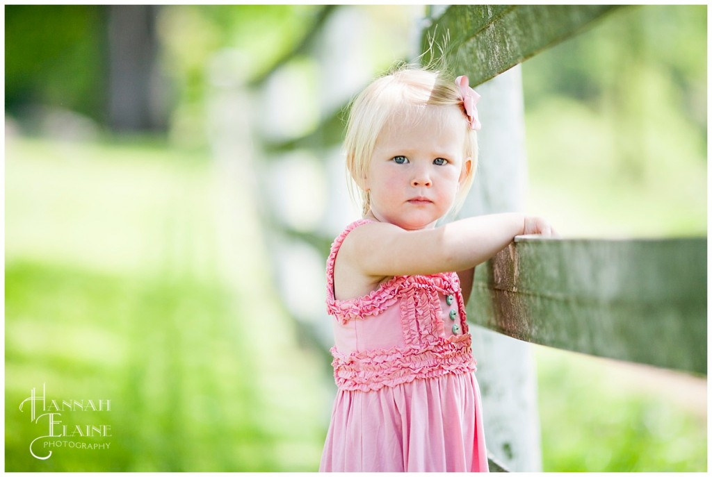 ellie leans against a dirty white fence