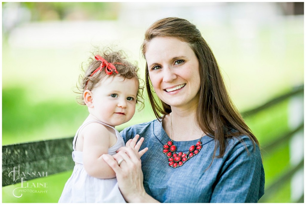 mom in denim dress holds baby girl with red bow