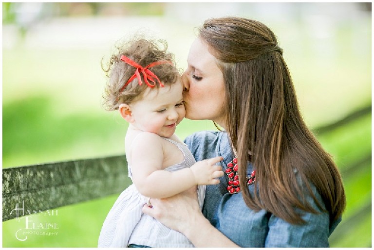 mom in denim dress kisses her baby girl on the cheek
