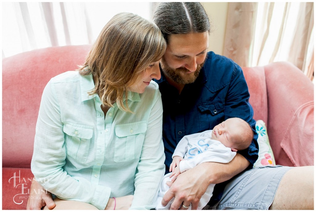 couple holding their newborn son on a pink velvet couch