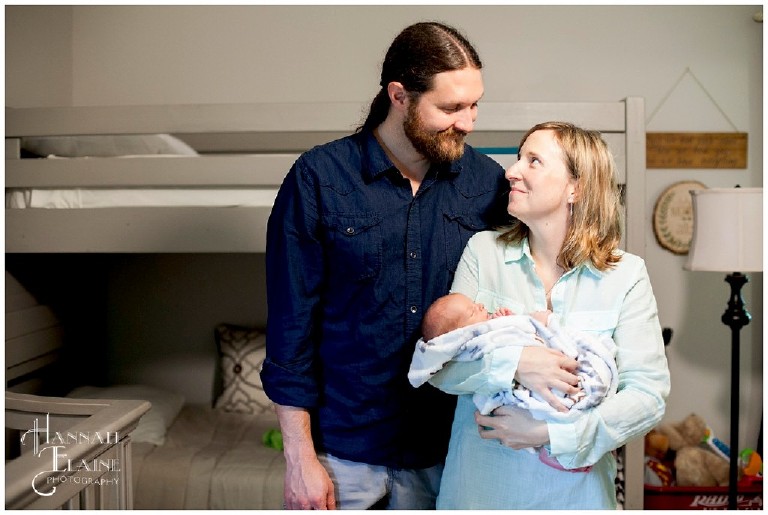 couple gazes at each other with newborn in their arms