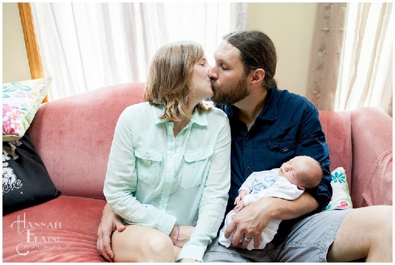 couple holding newborn baby give each other a kiss