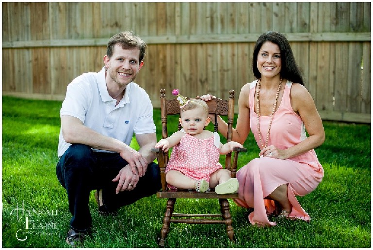 mom and dad squat next to baby girl in vintage rocking chair