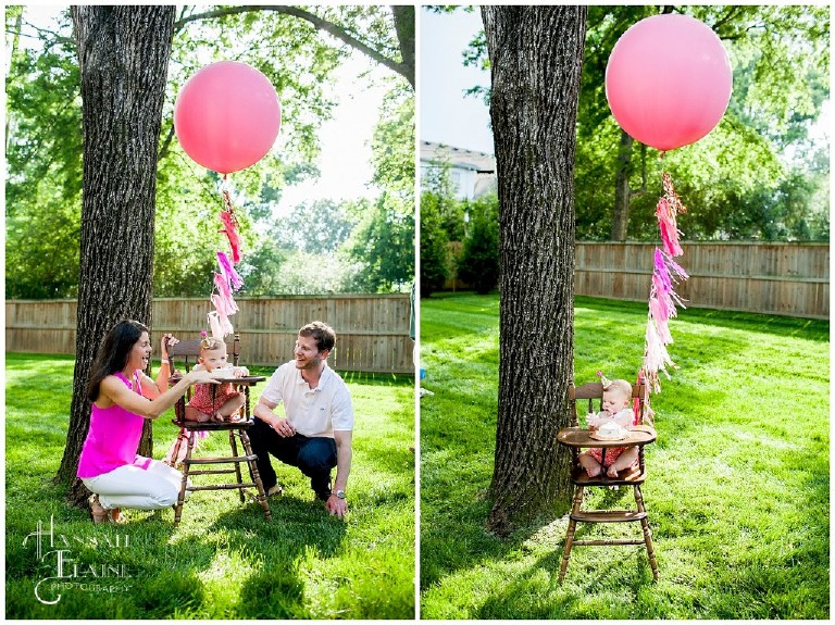 one year old in vintage high chair eats cake flanked by giant pink balloon