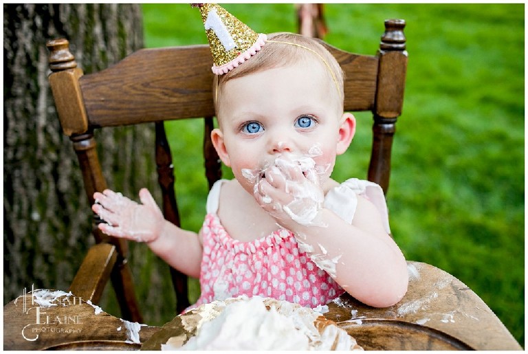 blue eyed baby girl in party hat smashes cake in her face