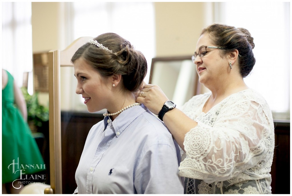 mom helps put pearl necklace on the bride