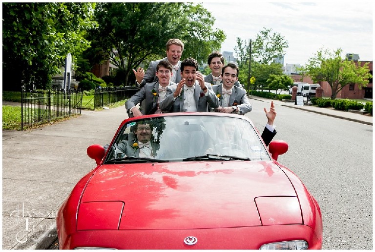 the boys in the bridal party squeeze into a tiny red car