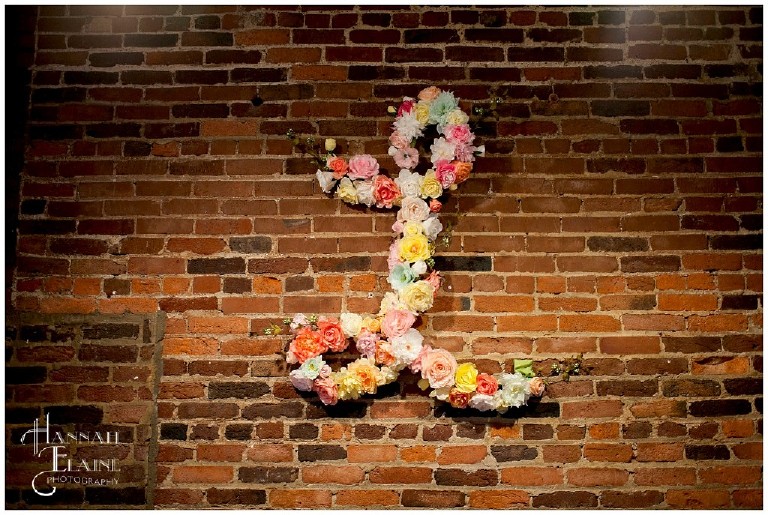 L monogram covered in bright flowers hanging on brick wall