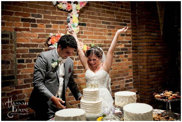 bride throws her hands up as groom serves the first piece of cake