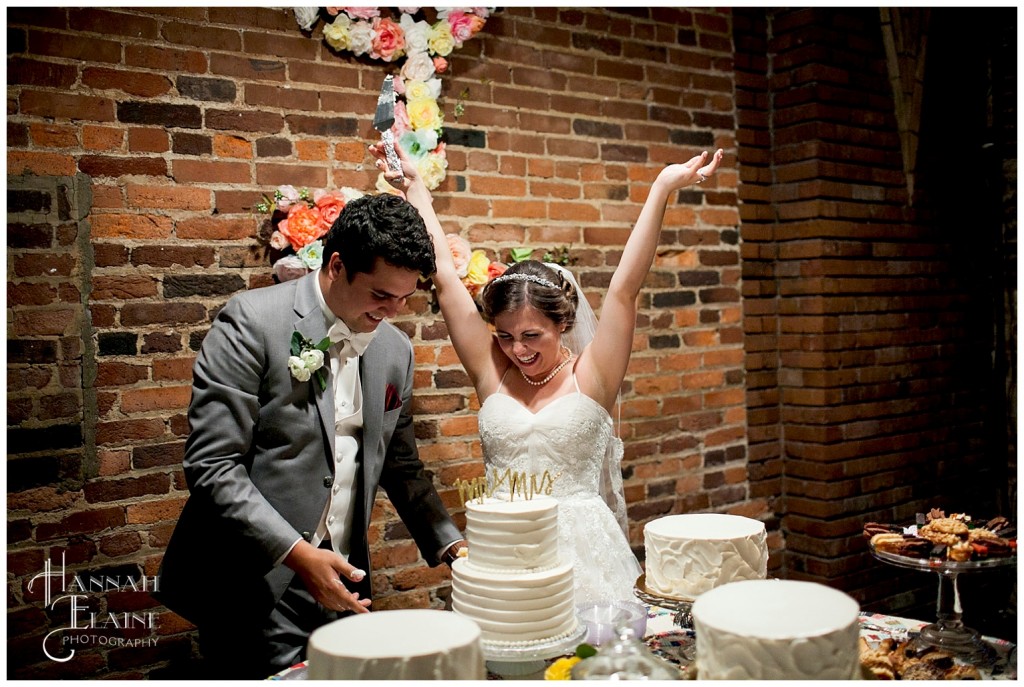 bride throws her hands up as groom serves the first piece of cake