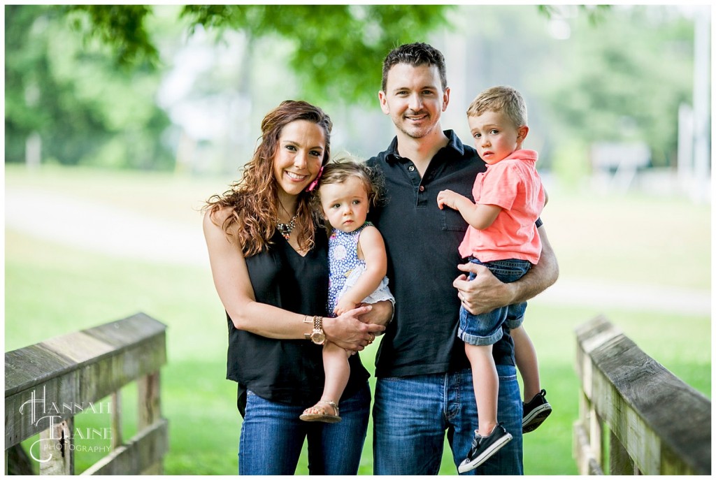 cute family poses together on a bridge in the park