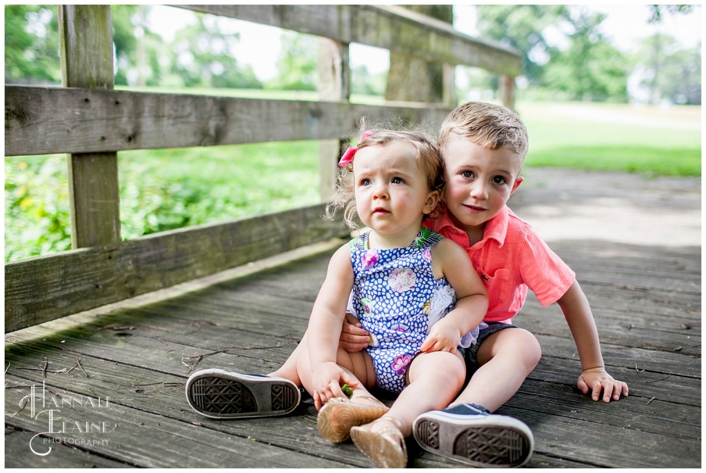 boy and girl sit together on a wooden bridge