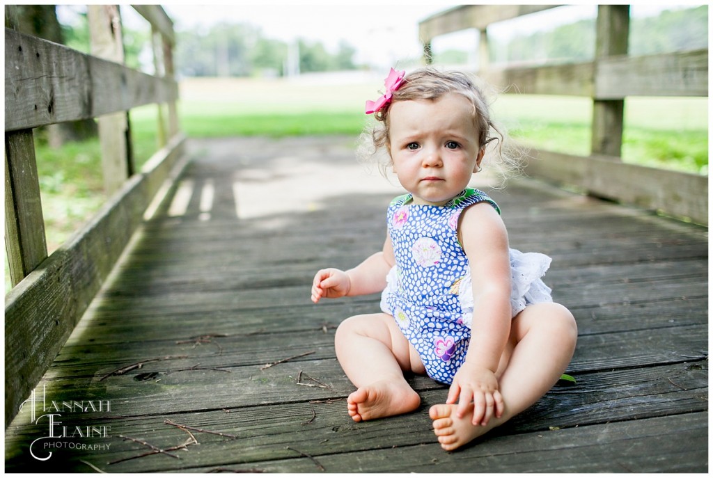 little girl in blue jumper sits on a wooden bridge