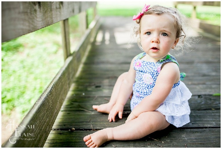 little girl with cute chunky legs sits on a wooden bridge