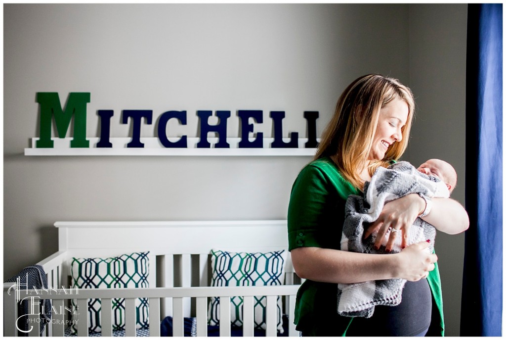 mom holds baby in front of crib with monogram sign on wall