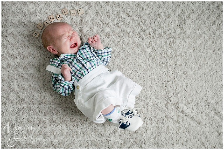 baby in sunday best lays next to scrabble letters