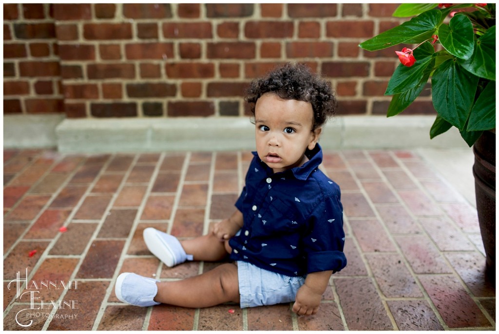 curly haired boy sits in the bricks in his summer clothes