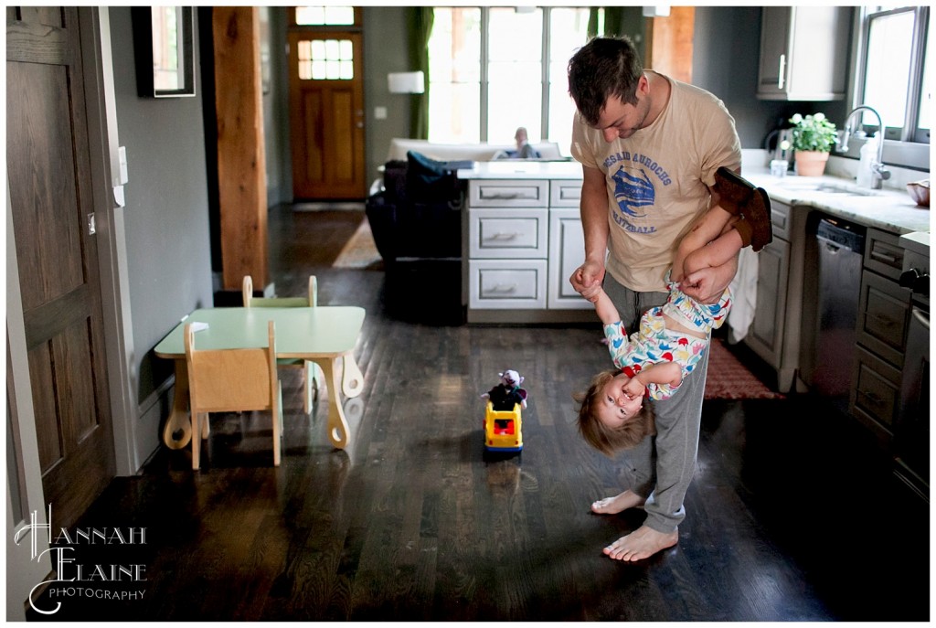 candid photo of dad swinging baby girl upside down